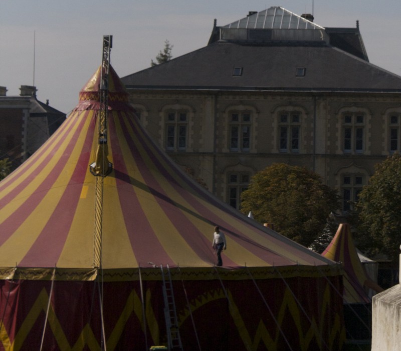 Chapiteau à rayures rouges et jaunes en premier plan, il y a un bonhomme sur le toit derrière : un bâtiment du XIX ème siècles ?